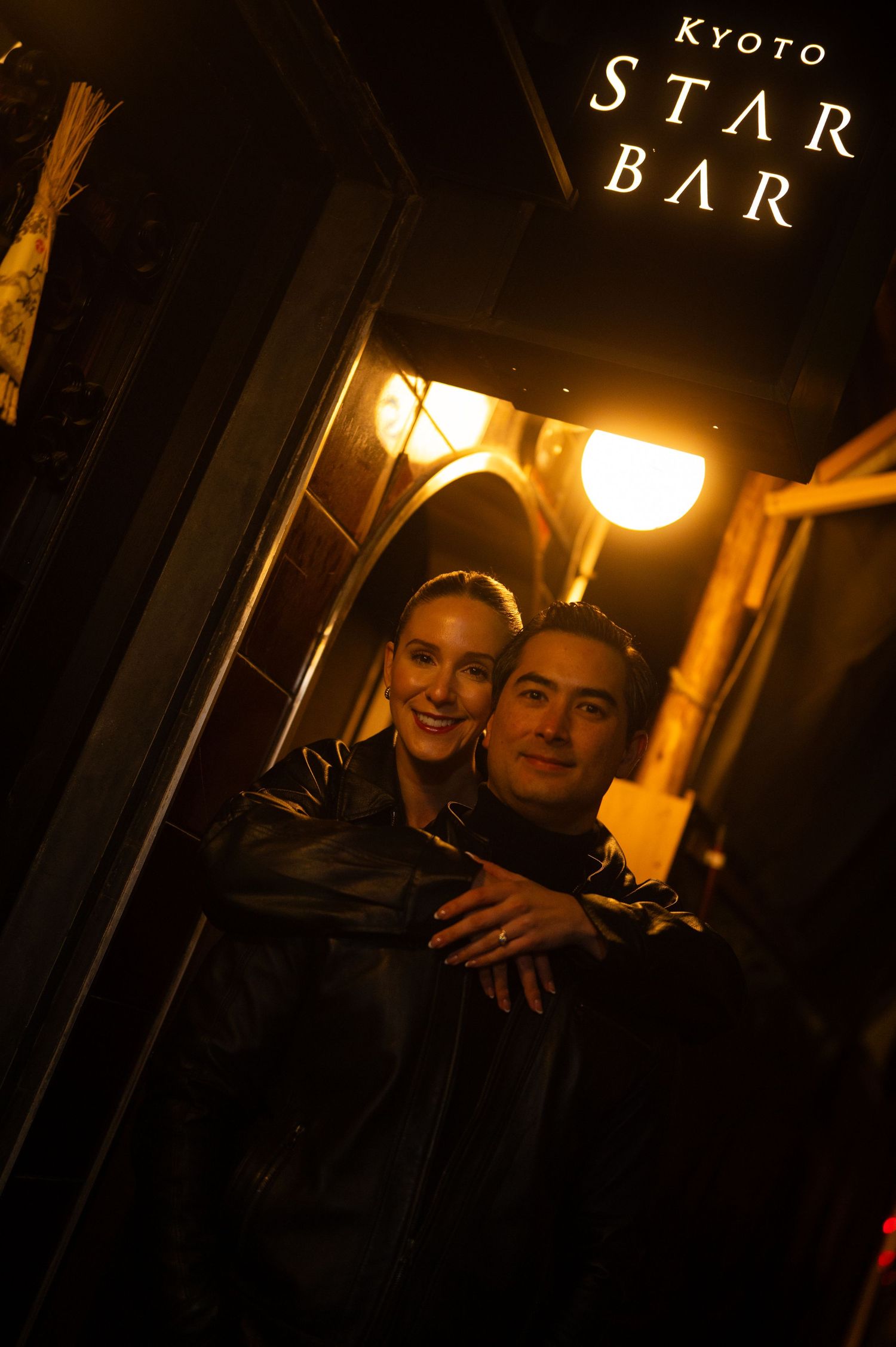 Couple embracing outside Kyoto Star Bar at night, bathed in warm golden light.