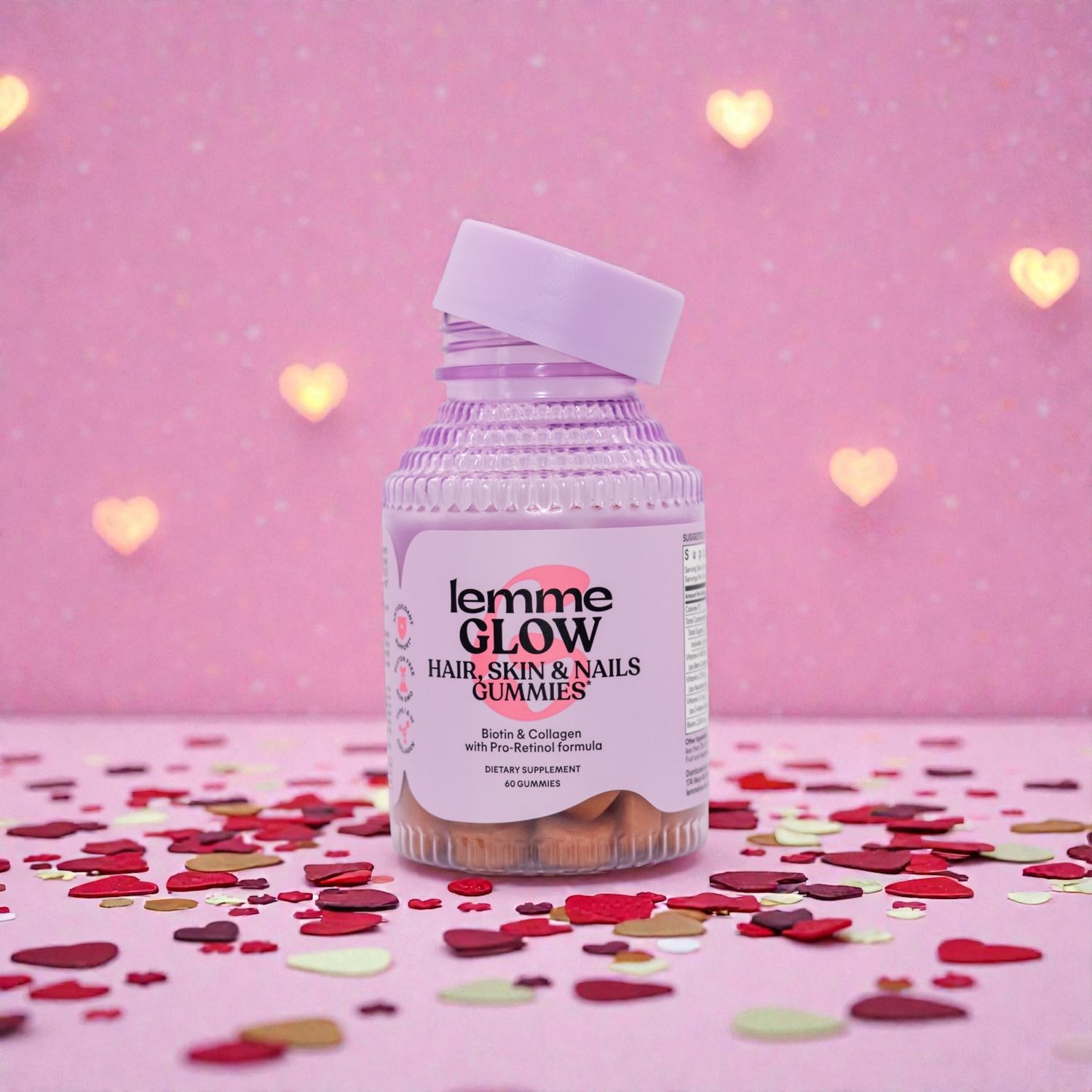 A bottle of Femme Glow vitamins on pink background with heart bokeh and red confetti scattered around.