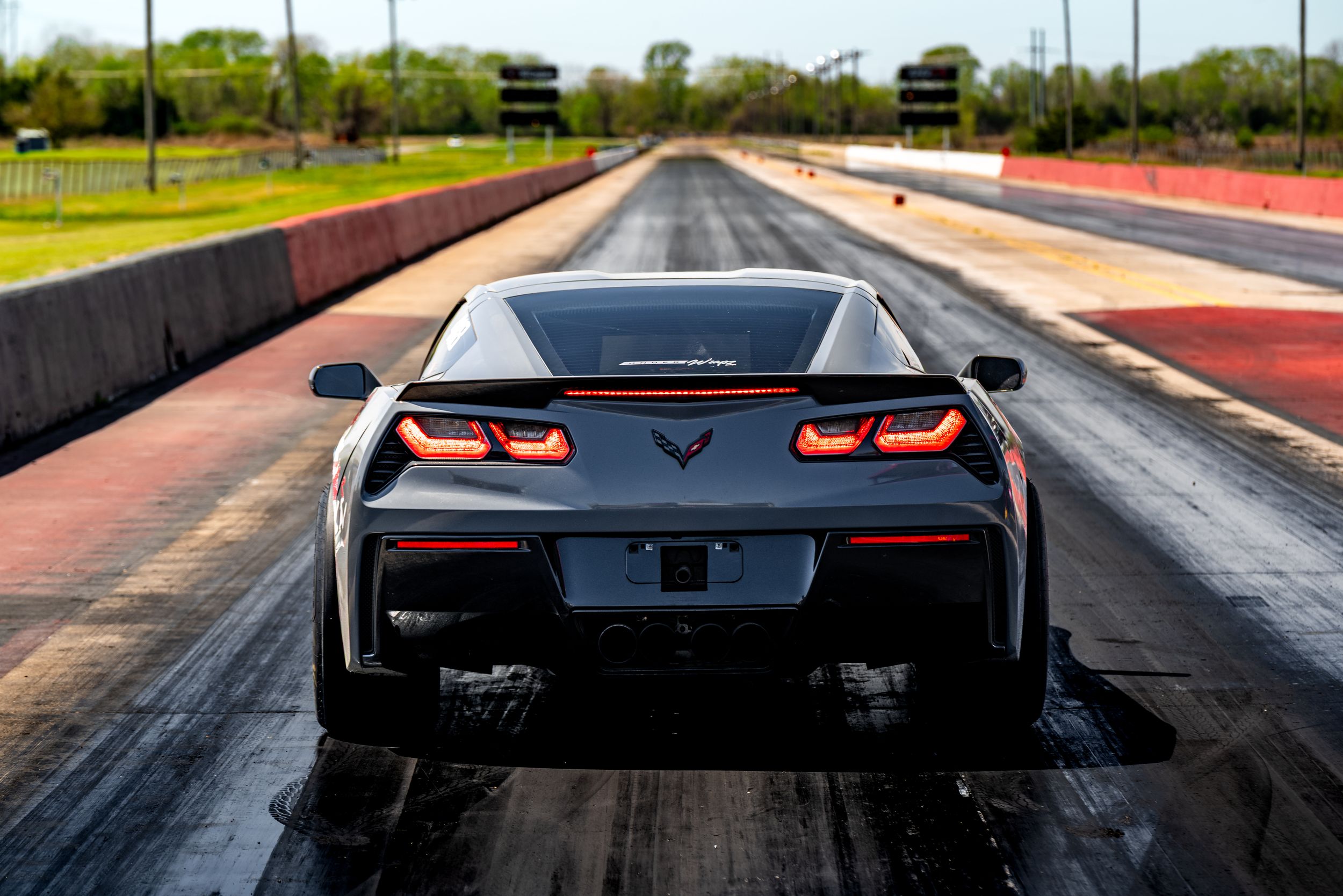 A series of seven photos showing a black Corvette from different angles on a racetrack during sunset.