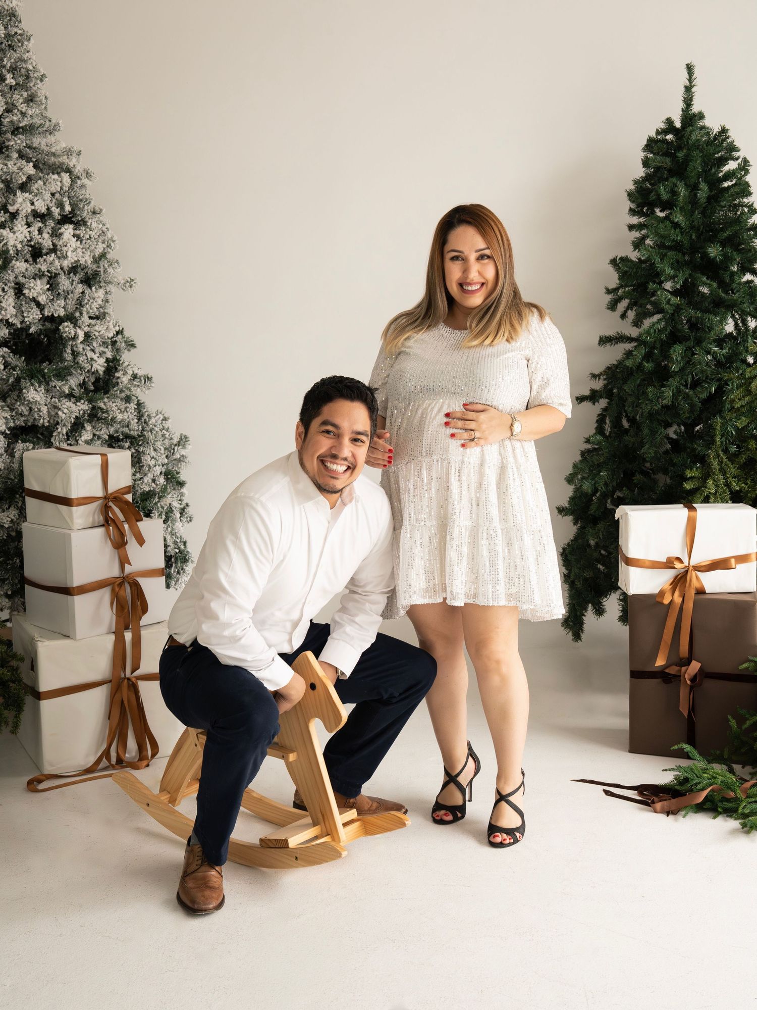 A couple poses playfully in a white studio with Christmas decorations and a rocking chair.