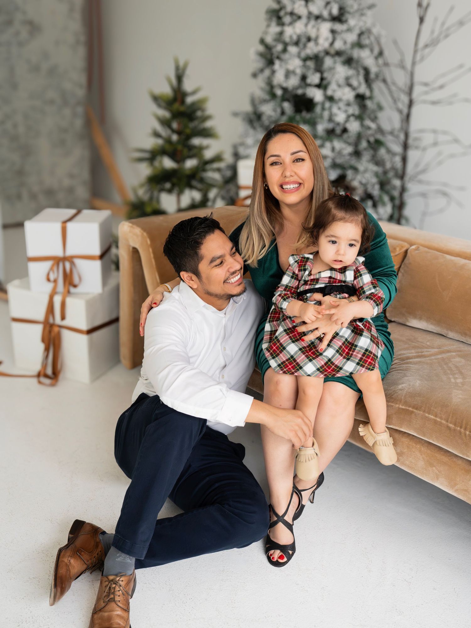 Family shares joyful moments in a holiday-themed photo session with Christmas trees and white decor.
