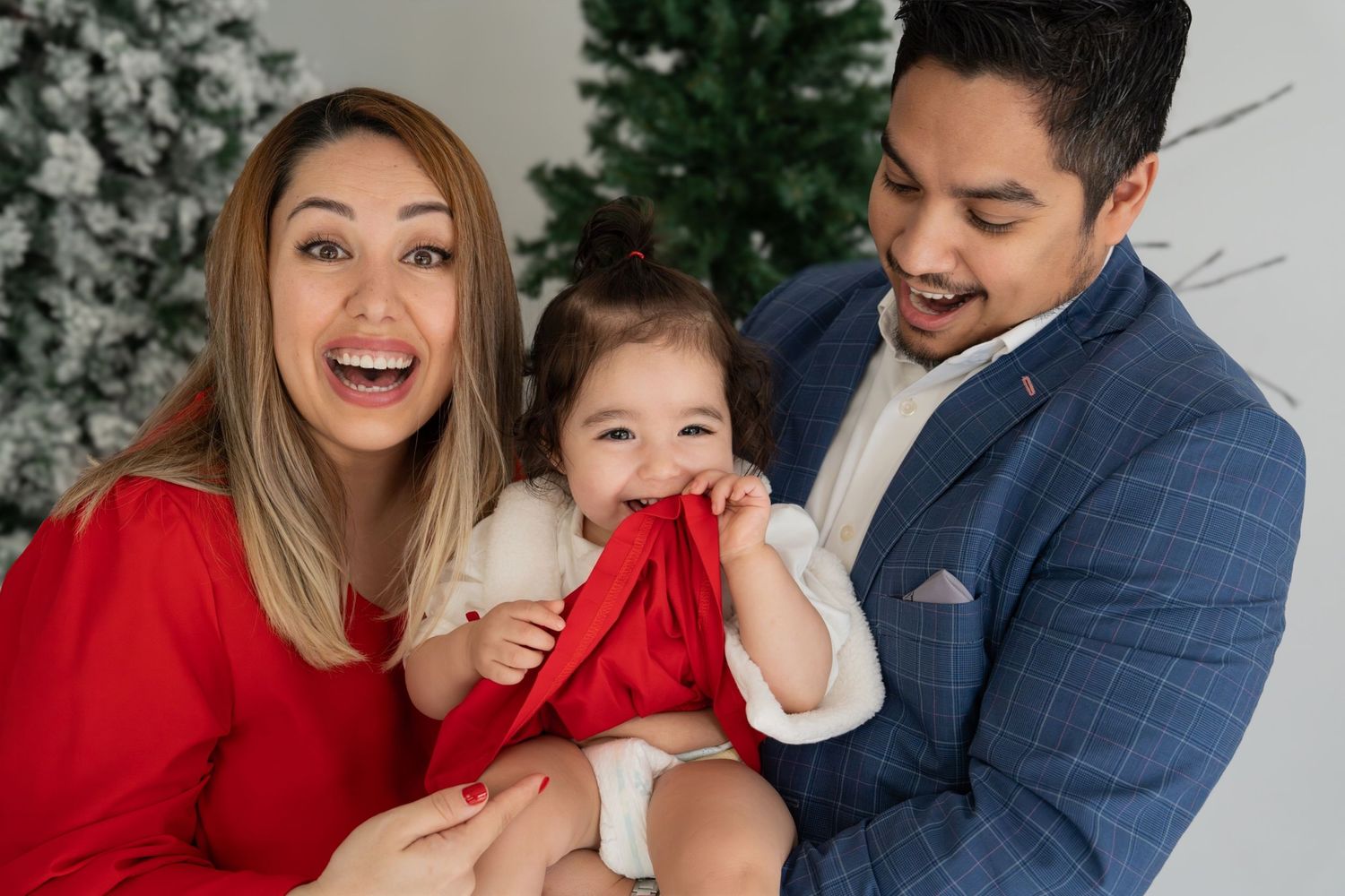 A happy family wearing red and navy outfits poses together for holiday photos in a studio setting.