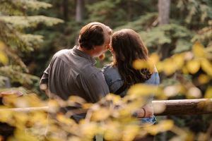 A couple holding hands while walking through a sunlit forest with golden autumn leaves.