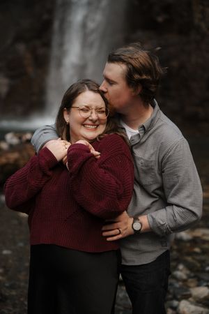 A couple shares intimate moments outdoors in autumn, wearing burgundy sweater and gray jacket while embracing.