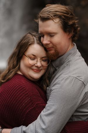 An intimate couple's portrait shows them sharing a tender moment against a moody dark background.