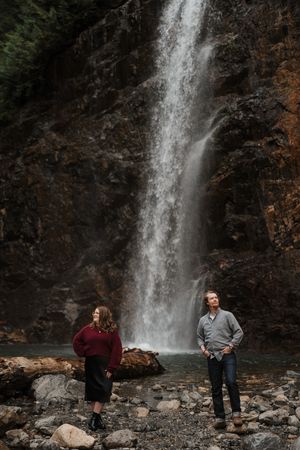A group of people pose near a majestic waterfall cascading down dark rocky cliffs in a scenic outdoor setting.