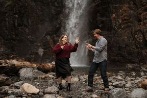 People gathered near a scenic waterfall in a forest setting.