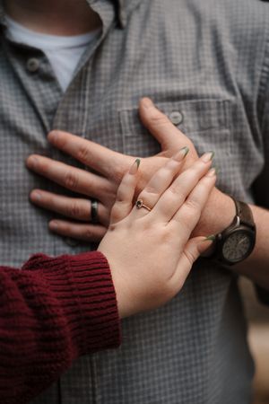A series of hands with wedding rings holding each other against a gray shirt and burgundy sweater background.