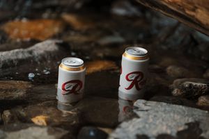 Several beer cans arranged on rocky ground in a natural outdoor setting.