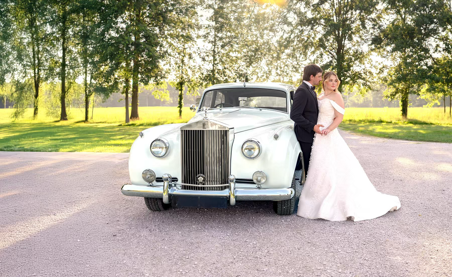 A classic white vintage car serves as a wedding vehicle in a sunny outdoor setting with trees and greenery at Jorgensen Farms