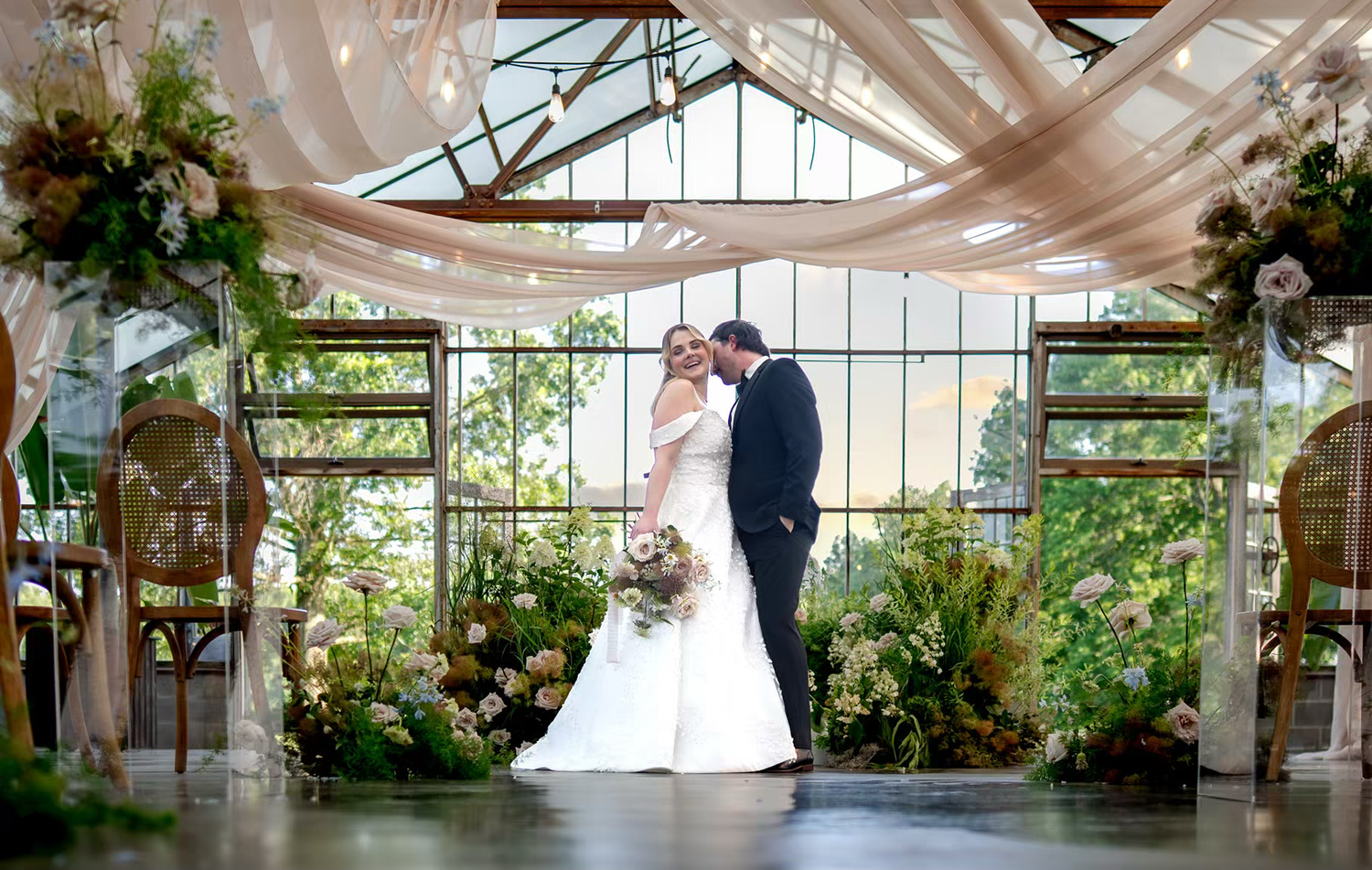 A panoramic view of a sunlit greenhouse wedding at Columbus Ohio Wedding venue with lush greenery and hanging floral decorations.