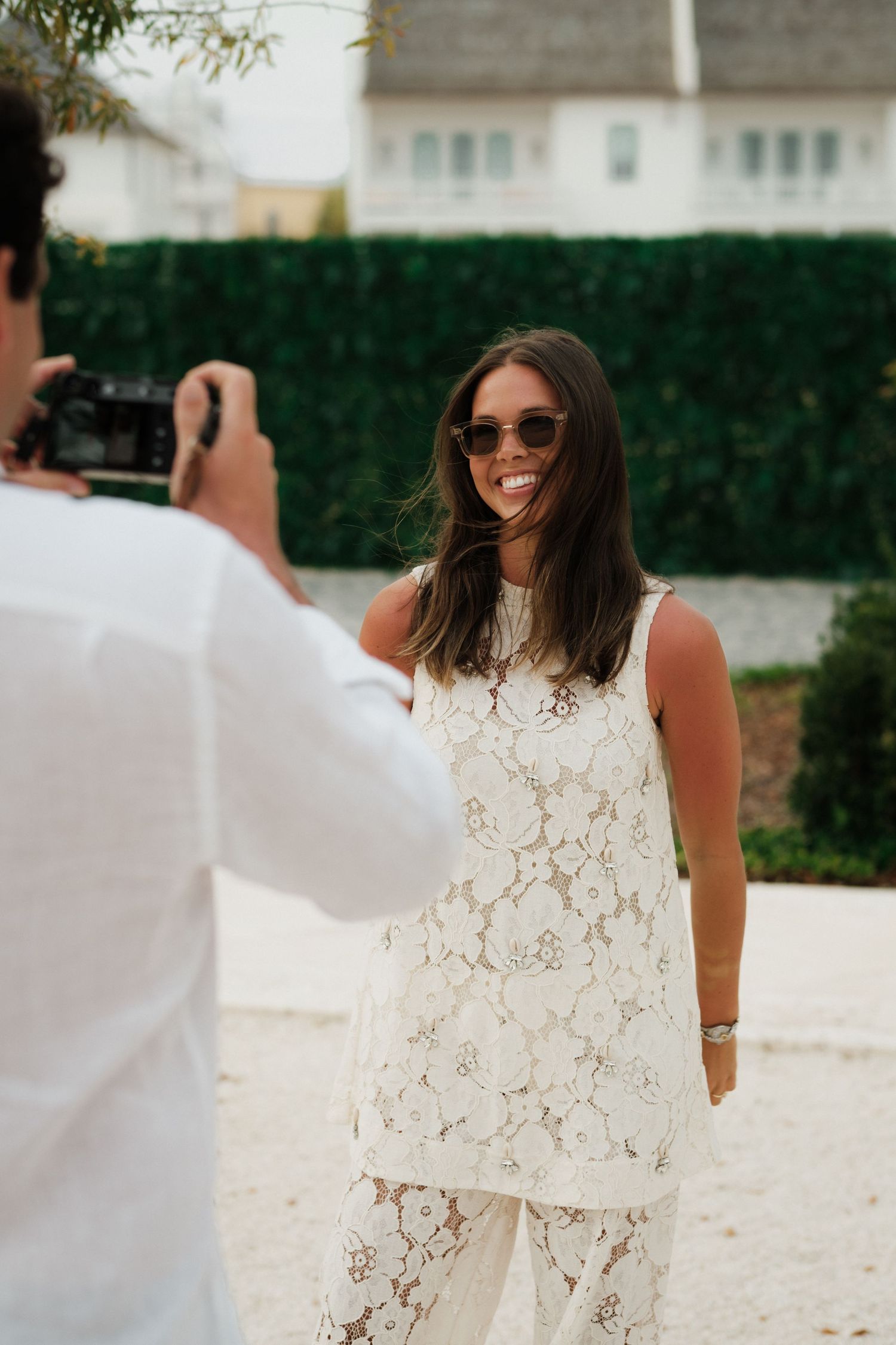 A person in white takes a photo of someone in a lace dress and sunglasses.