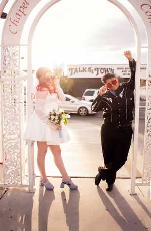 Little White Chapel Elopement LQBTQ couple leaning on gate pulling glasses down to nose