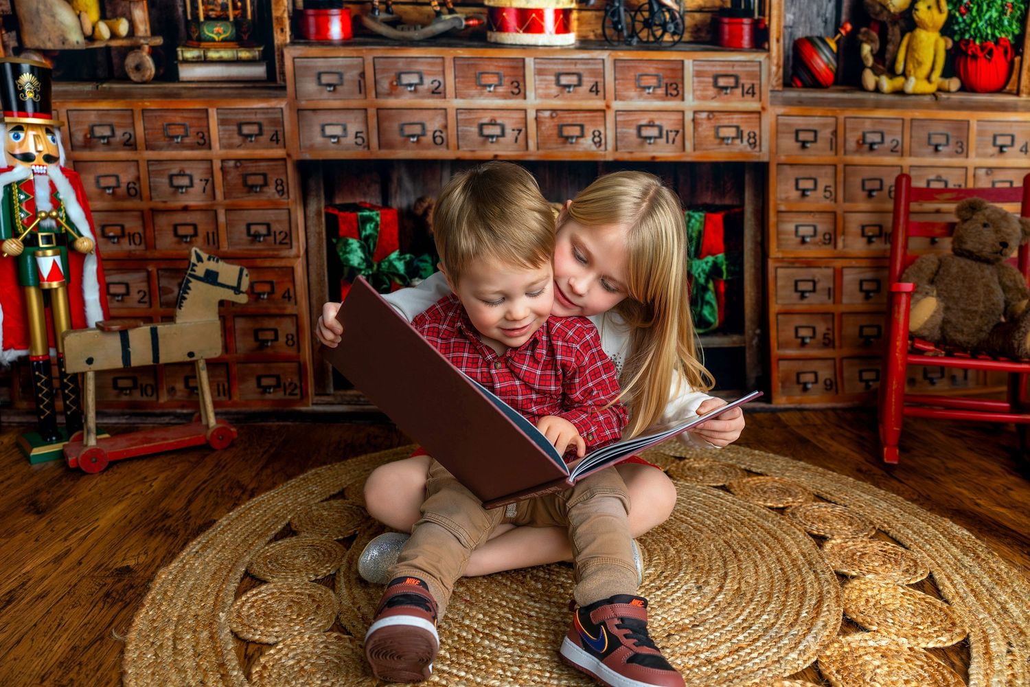 A young child sits on a woven rug while playing with colorful toys in front of wooden drawers and storage cabinets.