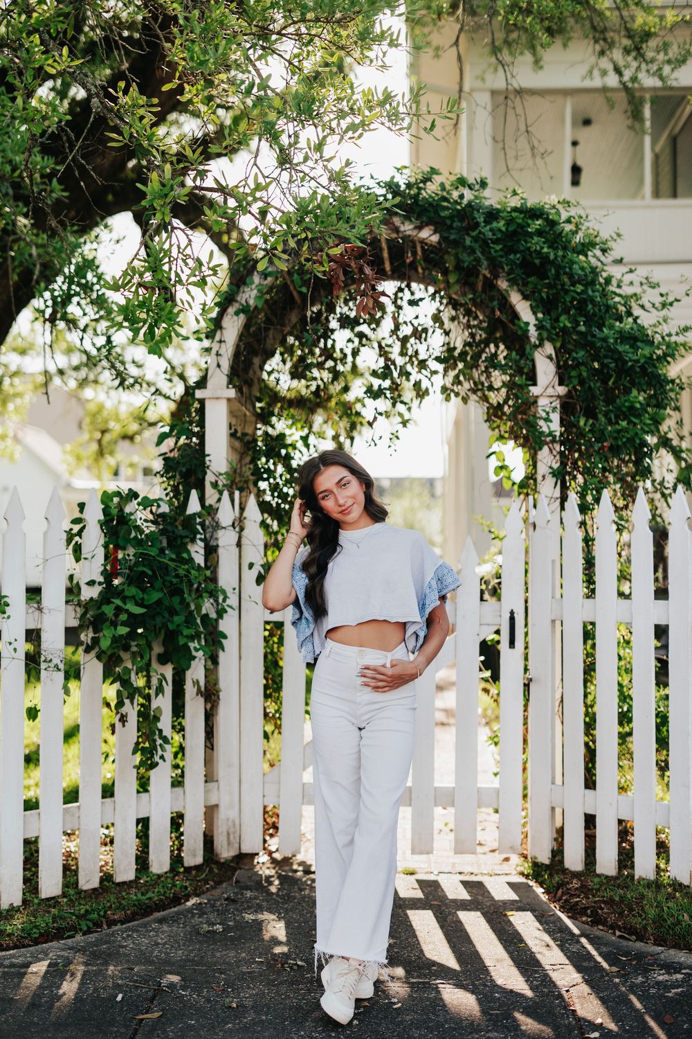 Fashion portrait against white picket fence with green vines and natural lighting.