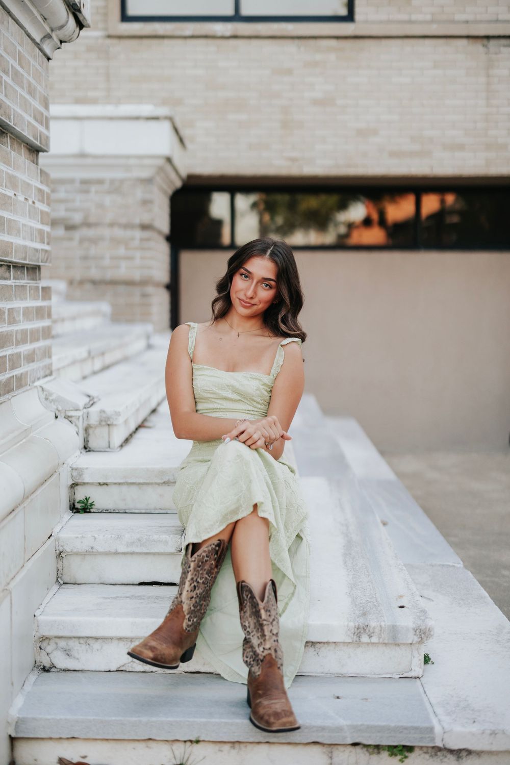 A light green sundress paired with brown cowboy boots creates a stylish contrast against white stone steps.