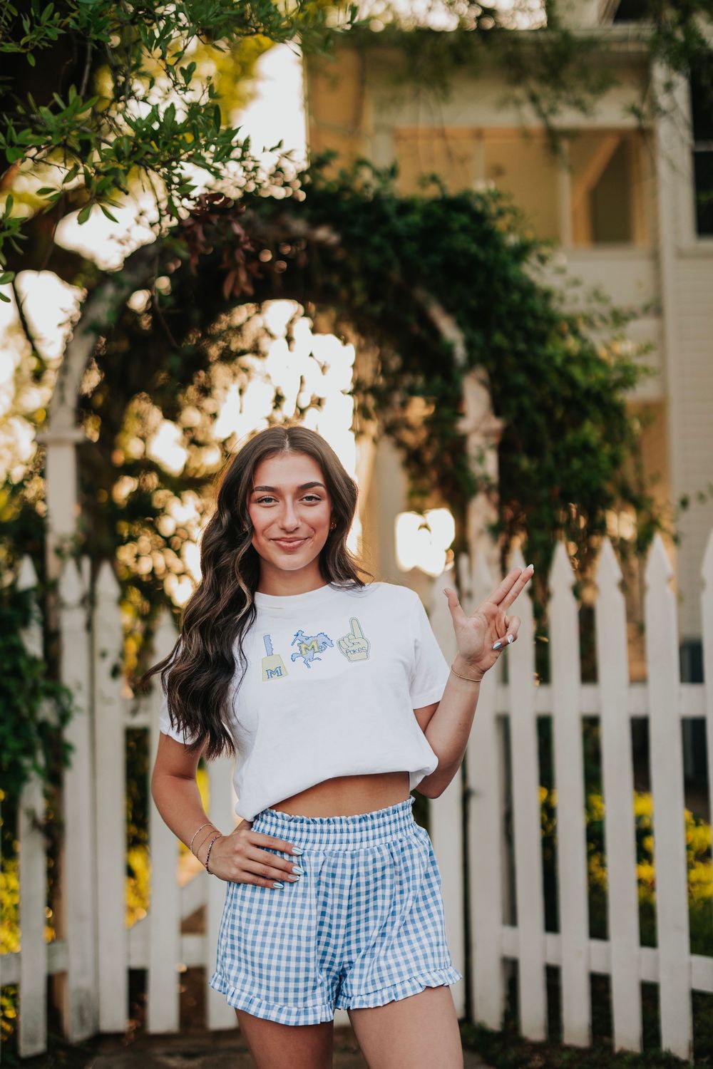 Summer fashion shoot by a white picket fence featuring blue gingham shorts and a graphic tee.