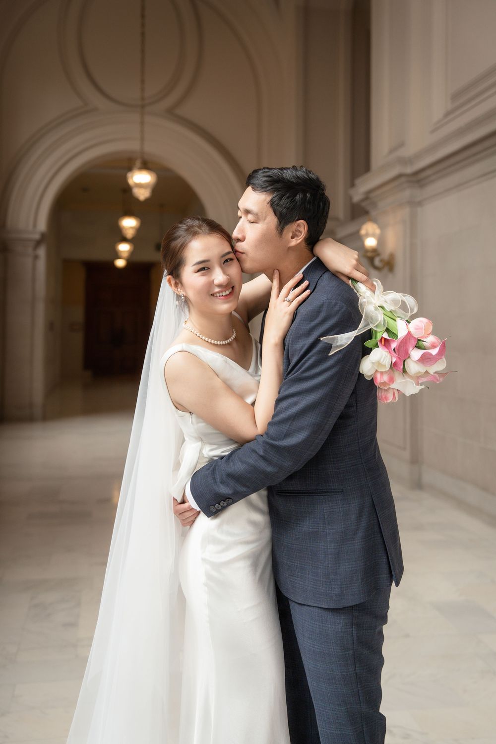 Romantic wedding couple shares intimate moments in an elegant hallway with ornate architectural details and hanging lights.