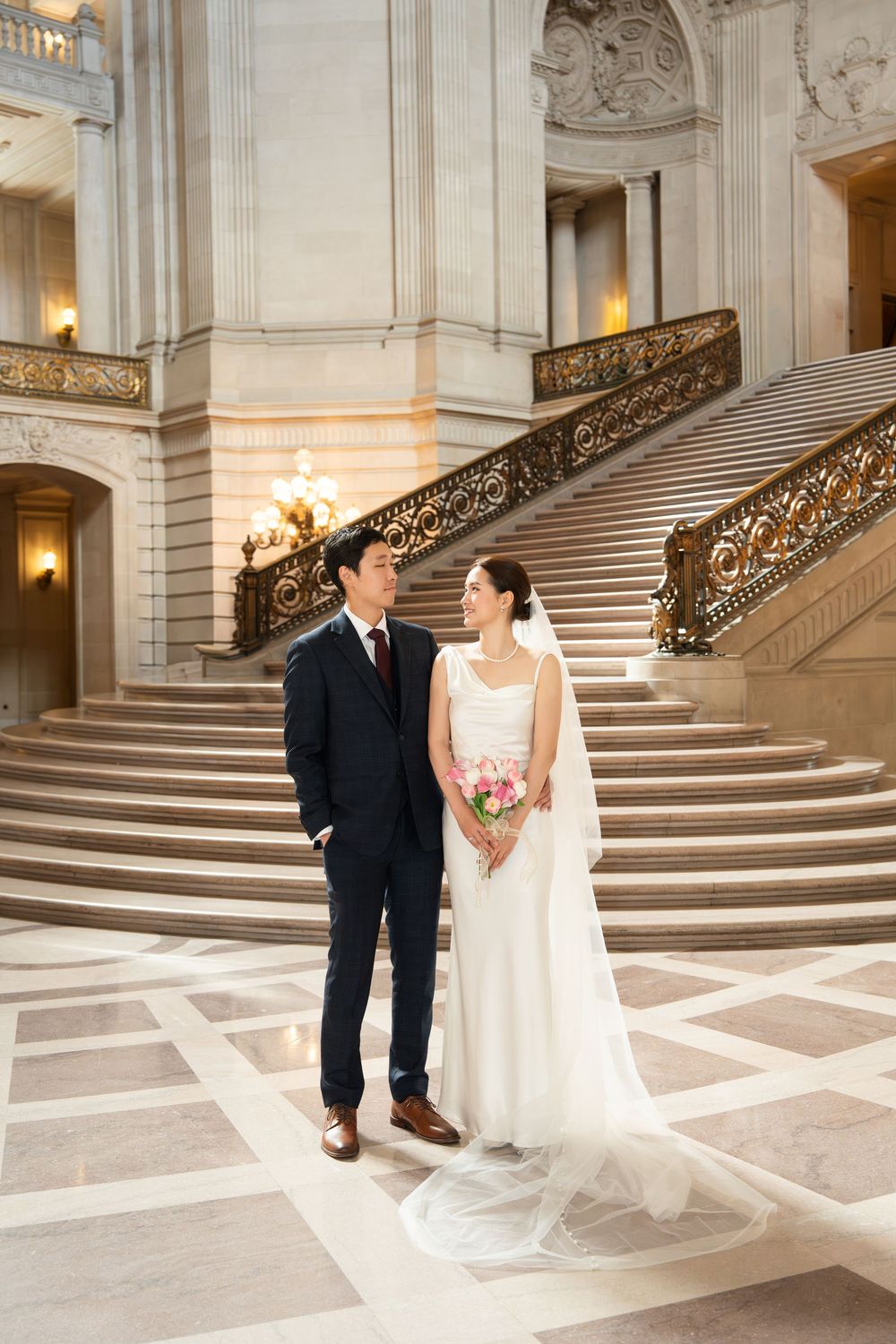 Elegant wedding photo series showing a couple posing on grand marble stairs with ornate railings in a historic building.