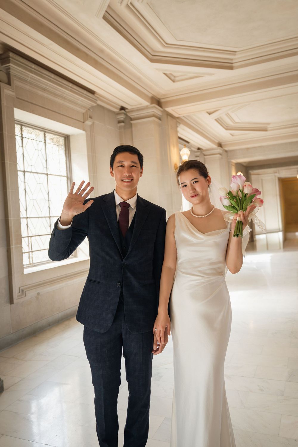 A bride and groom share joyful moments in an elegant white room with ornate ceiling details.