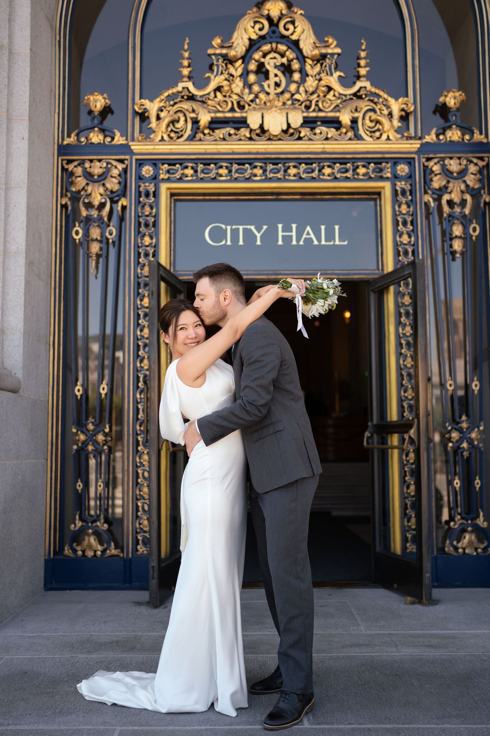 Wedding couple dancing in front of ornate gold gates at San Francisco City Hall entrance.