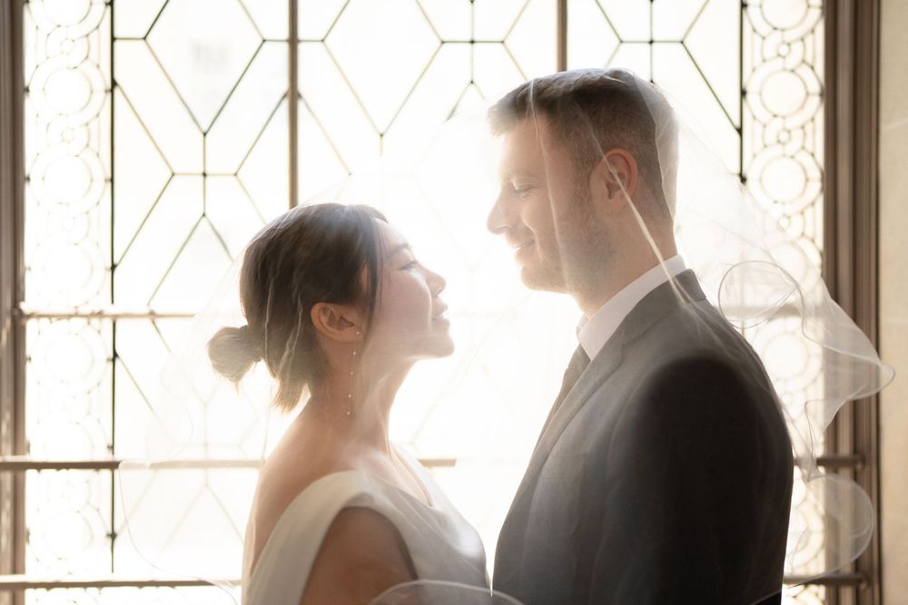 A romantic silhouette of a wedding couple standing by a geometric window with soft natural light.