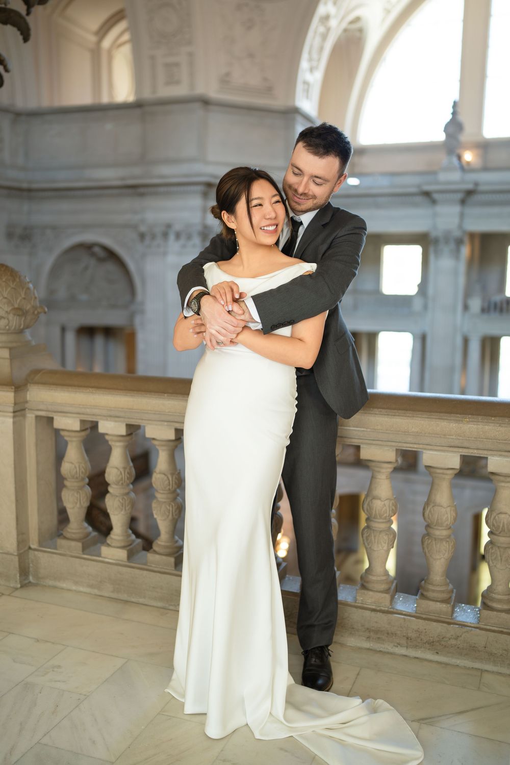 Romantic couple embraces near ornate stone balustrade in historic building.