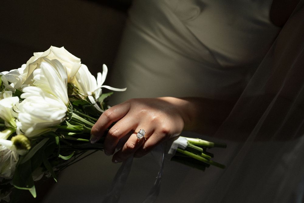 Close-up of white roses and hands with wedding rings in dramatic lighting.