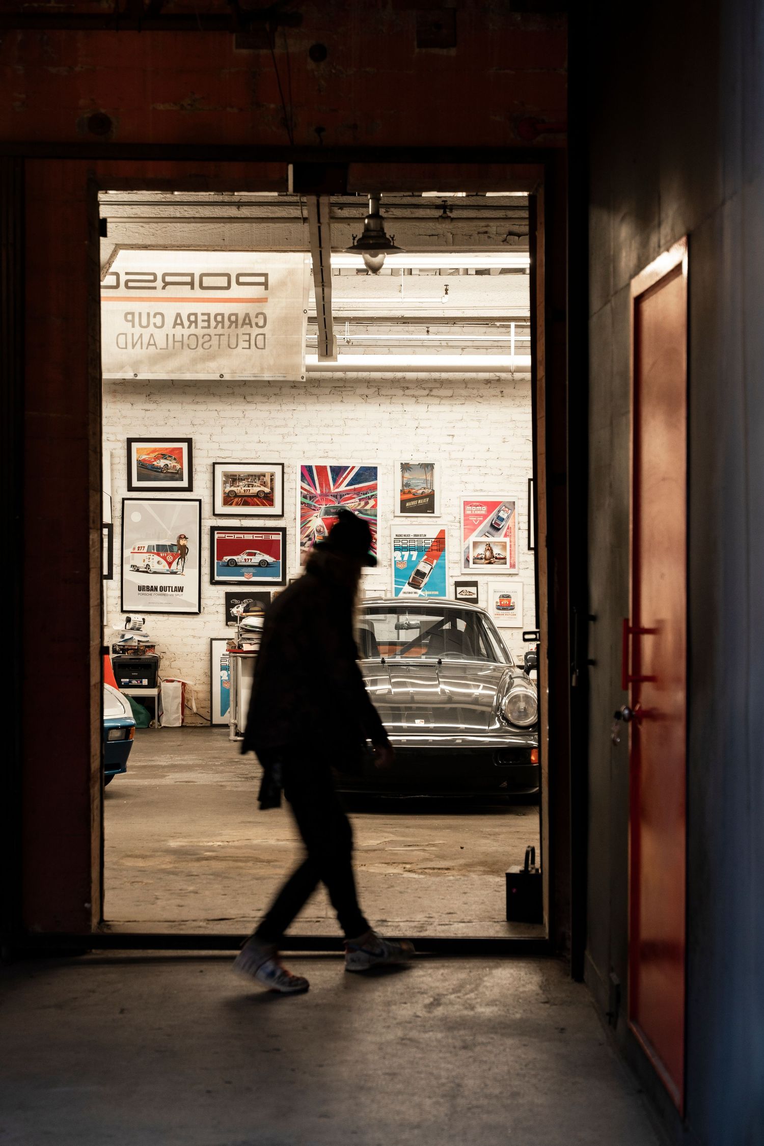 A sequence of silhouettes walking through a dimly lit parking garage entrance with posters on the wall.