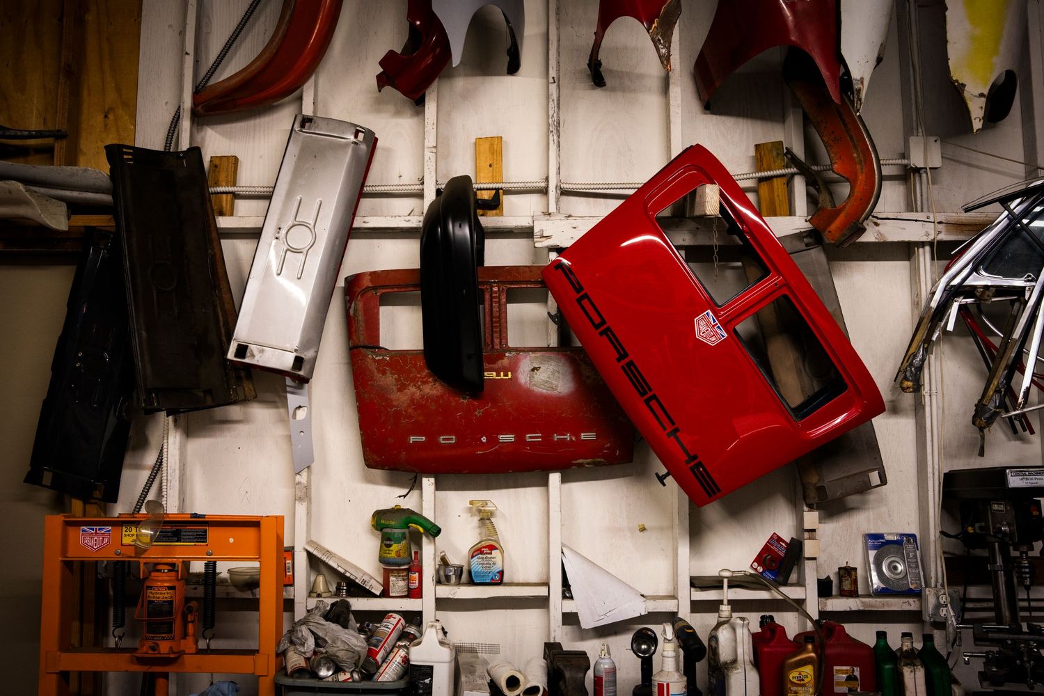 Cluttered workshop wall with hanging tools, equipment, and red storage containers in a disorganized arrangement.