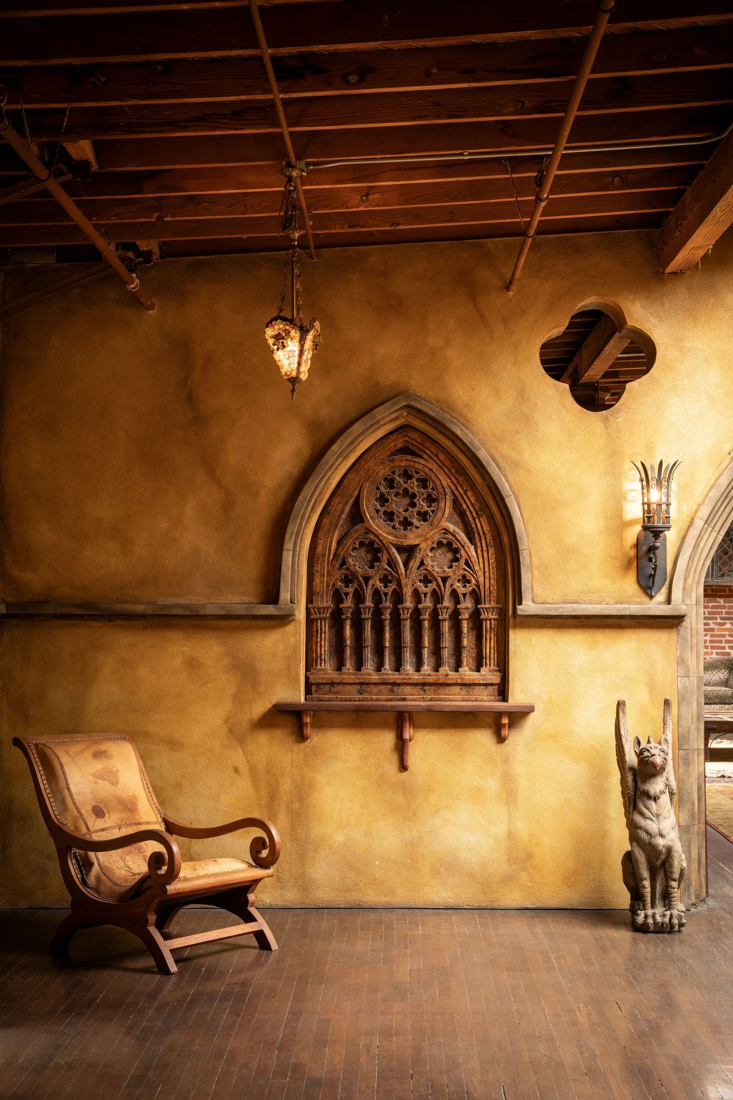 Medieval-style wooden bench seating along stone walls with Gothic arched windows in a historic castle interior.