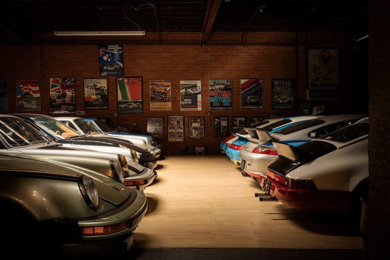 Classic Porsche sports cars lined up in a dimly lit garage with vintage posters decorating the walls.