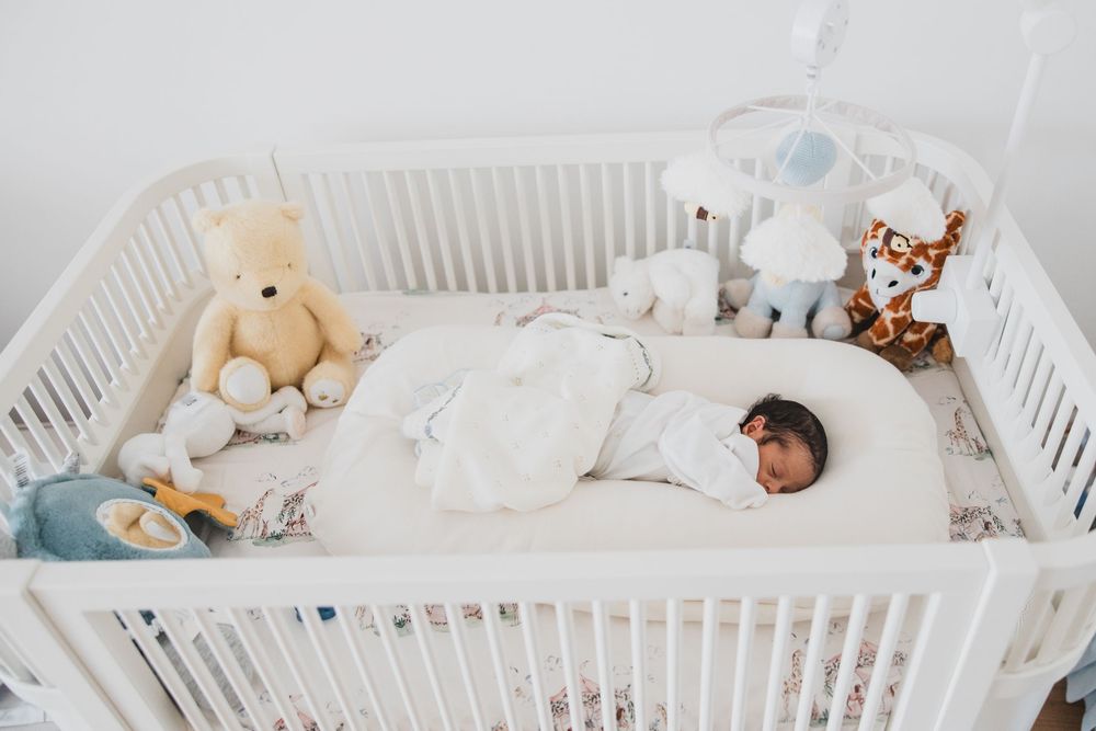 A white wooden crib filled with plush toys and soft bedding in a nursery setting.