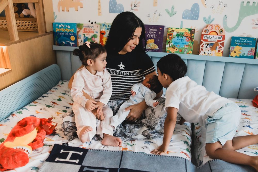 Children reading books together on a cozy bed with colorful wall decorations in a bright room.