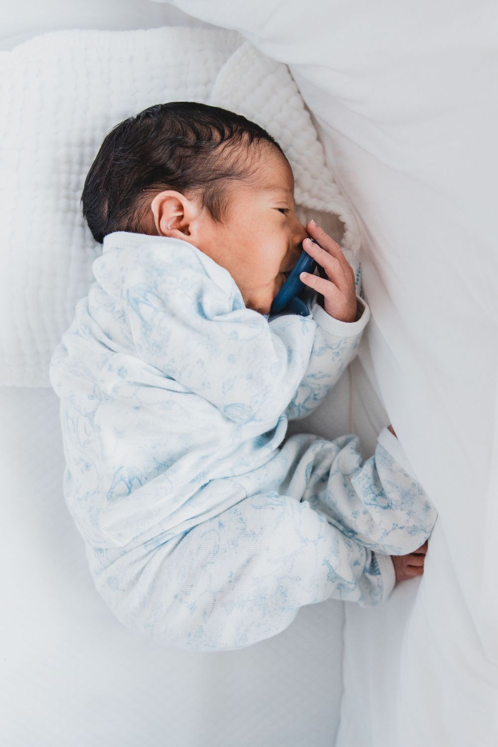 A sleeping newborn baby wrapped in a soft blue and white blanket lying on white bedding.