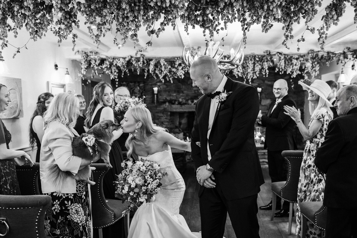 A group of wedding guests dance and celebrate under a white tent with hanging decorations and string lights.