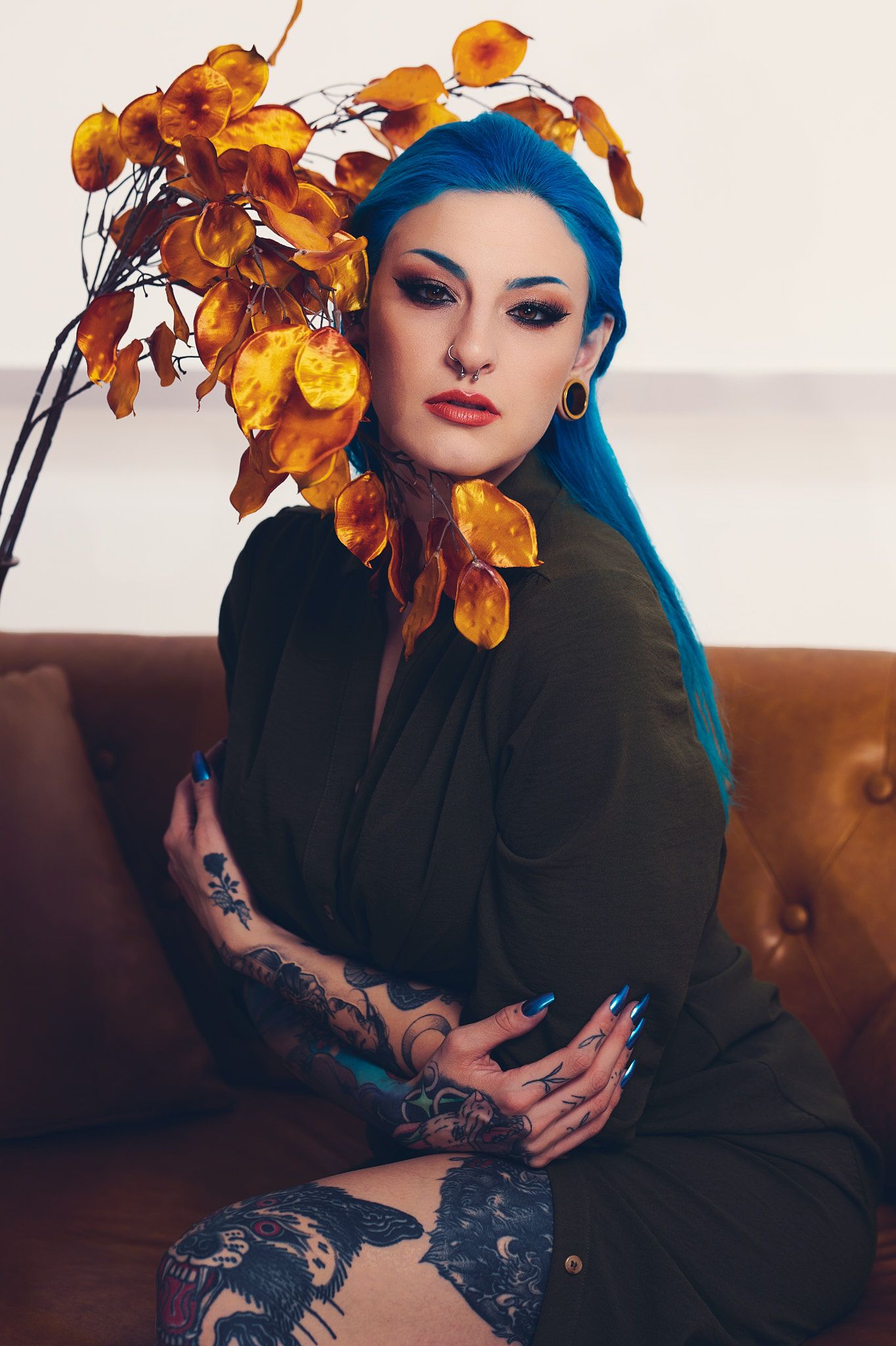 A gothic-inspired photoshoot featuring bright orange flowers and dark attire on a leather couch.