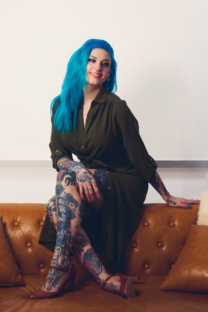 Alternative style portrait with bright blue hair against brown leather seating and white background.