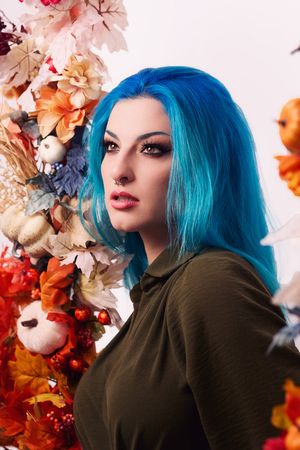 A portrait featuring vibrant blue hair against a backdrop of autumn-colored dried flowers and foliage.