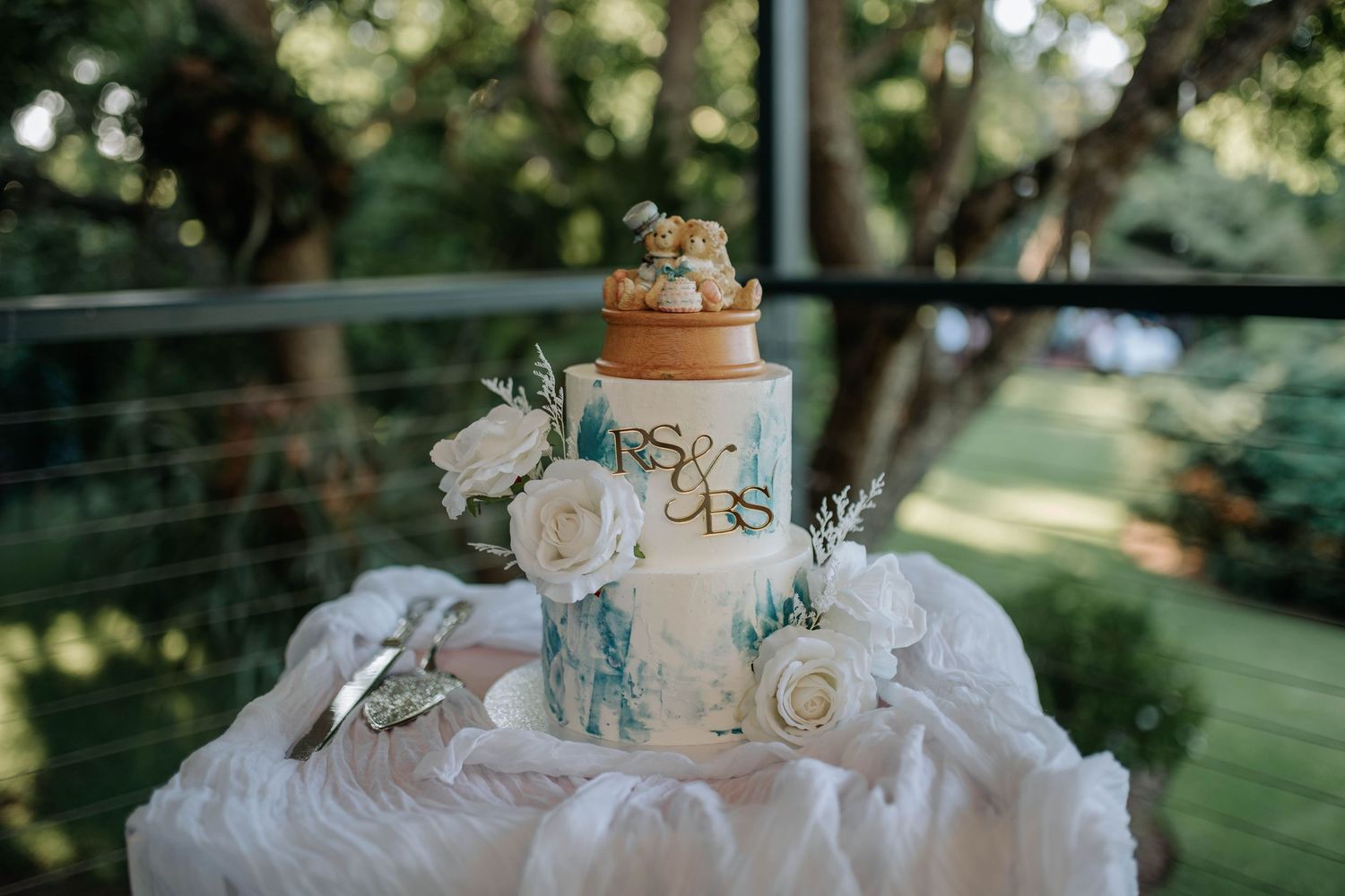 White wedding cake with delicate floral decorations and blue ribbon accents sits elegantly on display outdoors.