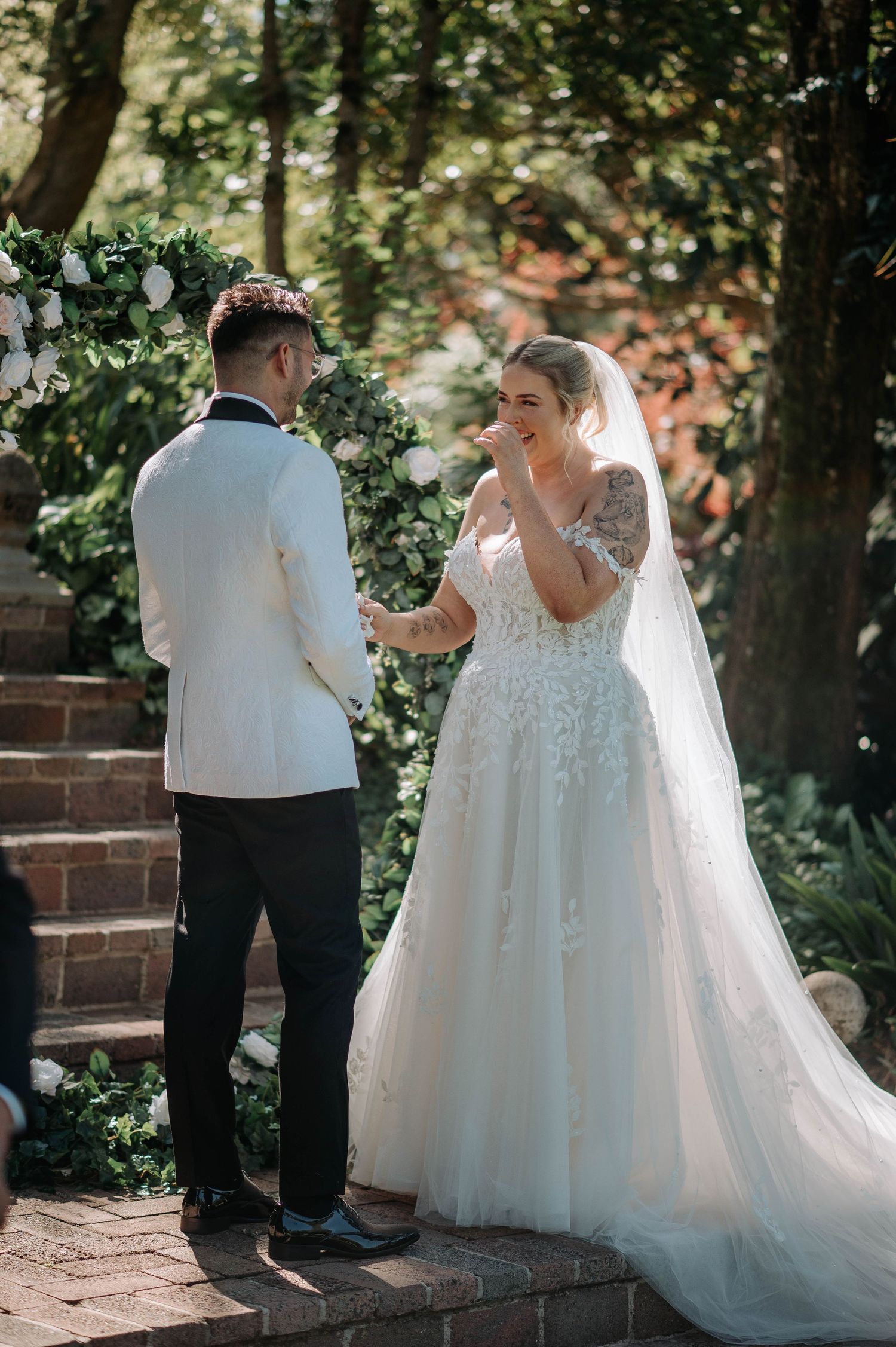 A tender first look moment between a couple in wedding attire on brick steps surrounded by greenery.