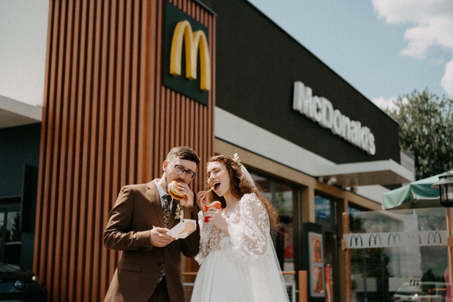 Newlyweds sharing ice cream cones and laughing together outside McDonald's restaurant.