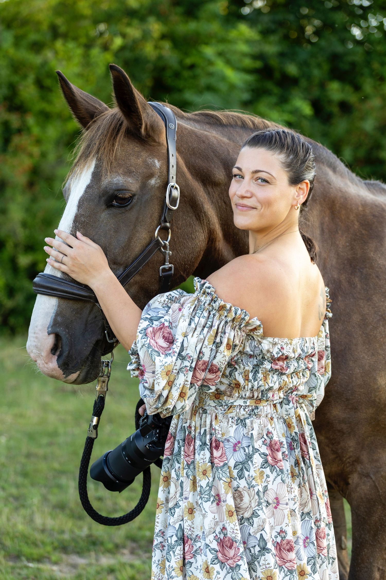 A dark brown horse stands next to someone wearing a floral off-shoulder dress in an outdoor garden setting during a photoshoot in Sydney