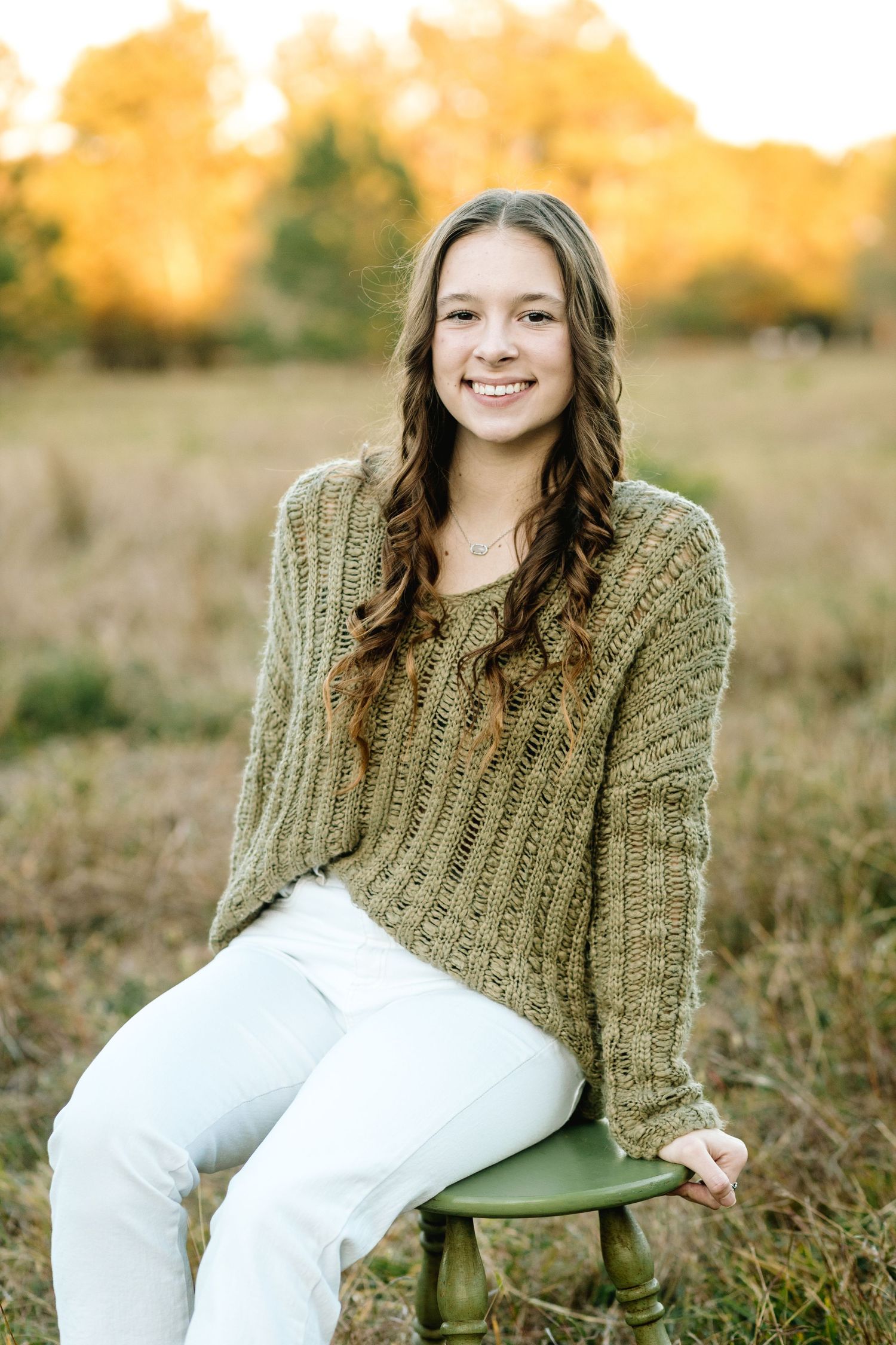 A series of outdoor portraits in a field with golden autumn colors and a green chair as a prop.