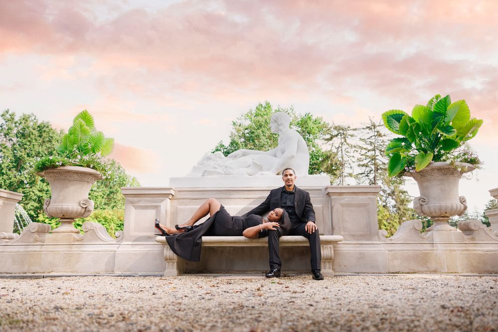 Person relaxes on outdoor bench surrounded by decorative planters at sunset.