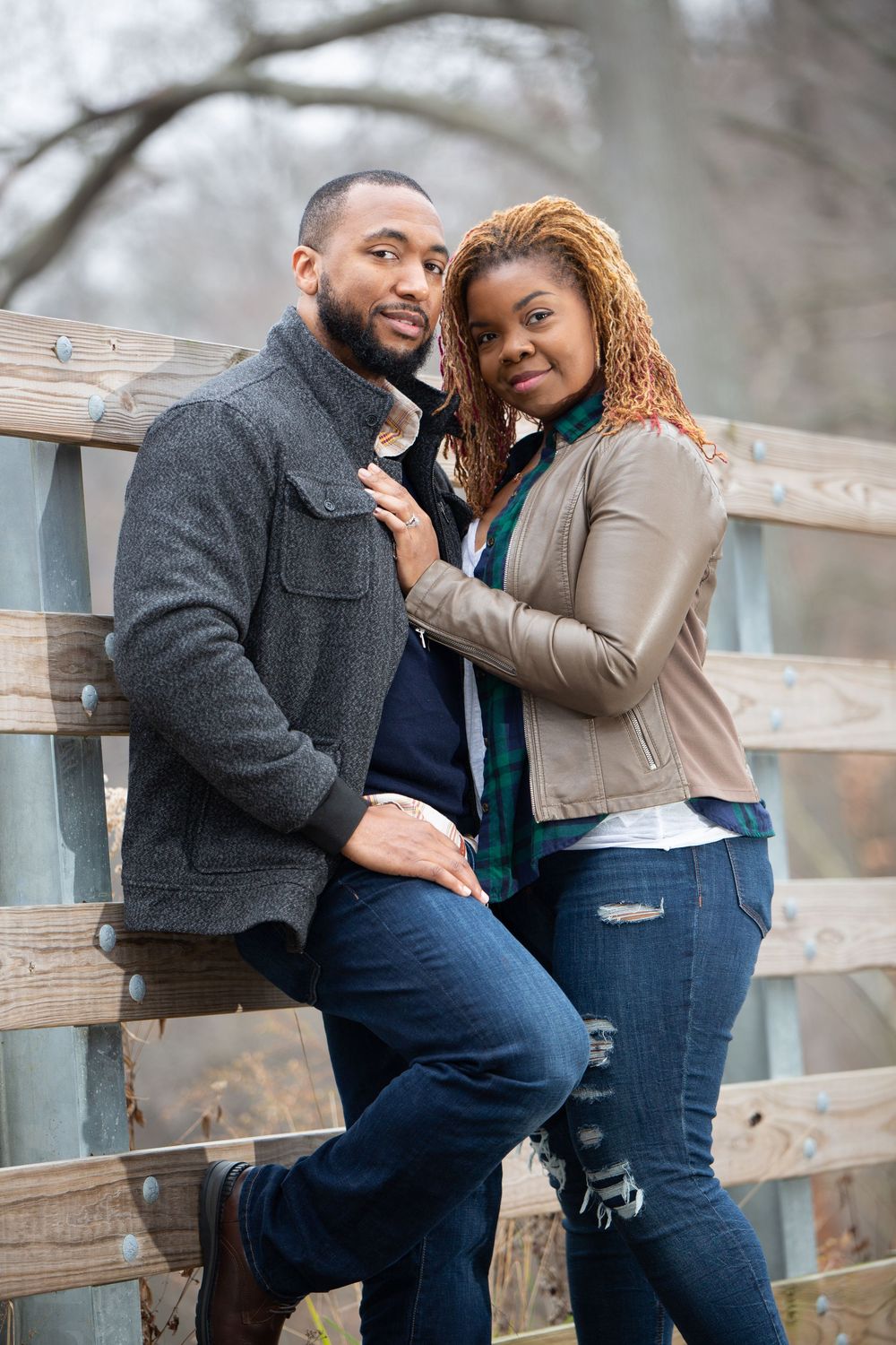 Couple shares intimate moments while posing on wooden railing during engagement photo shoot.