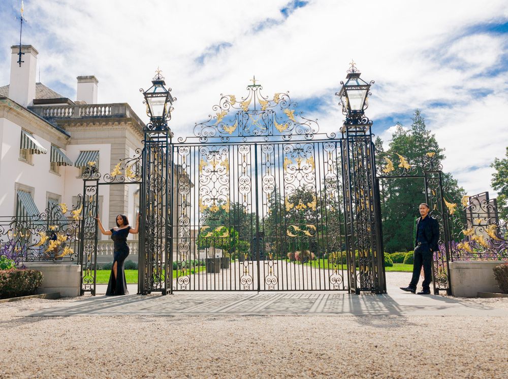 Silhouettes stand by ornate iron gates of grand estate entrance.