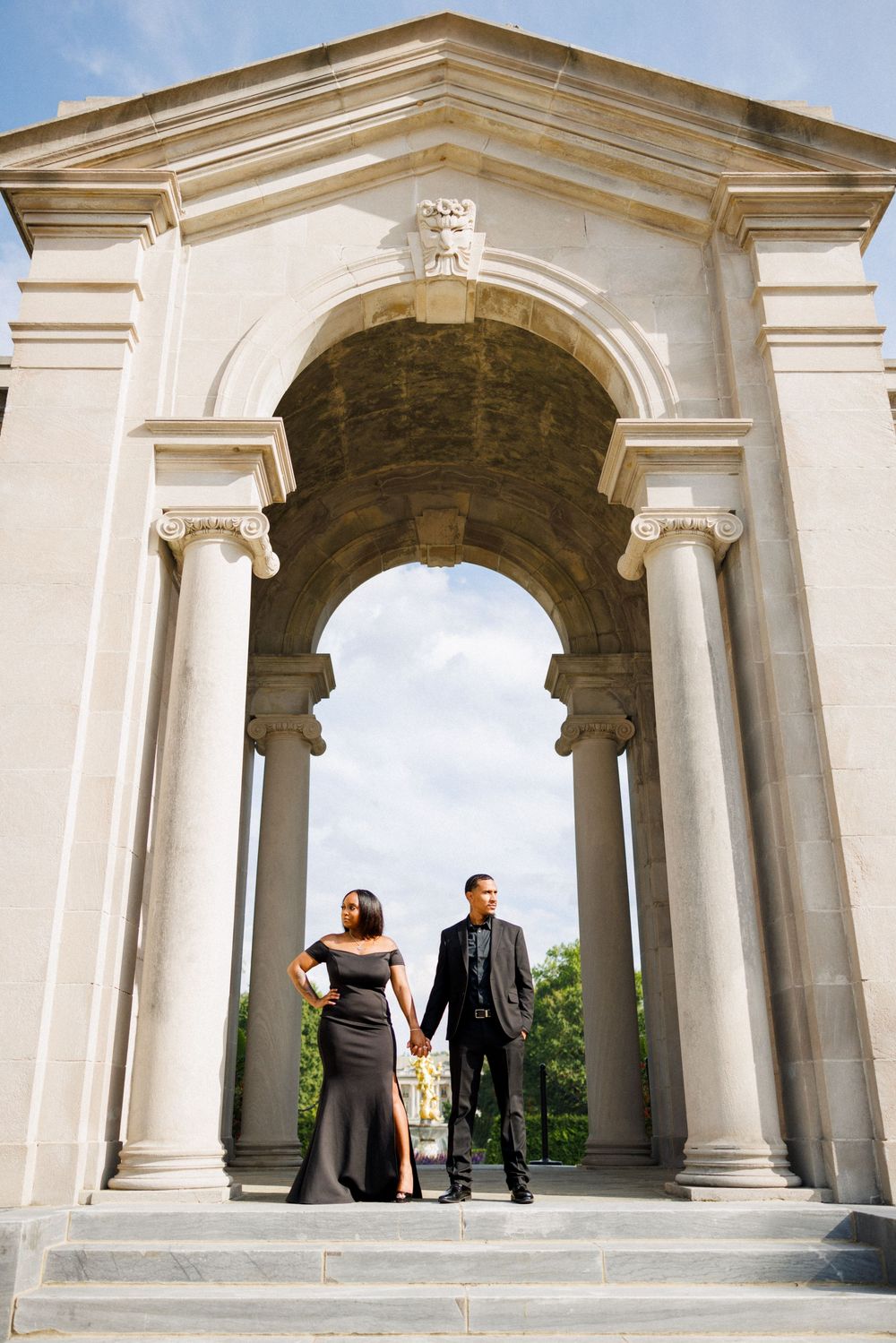 Couple holds hands while standing in elegant stone archway.