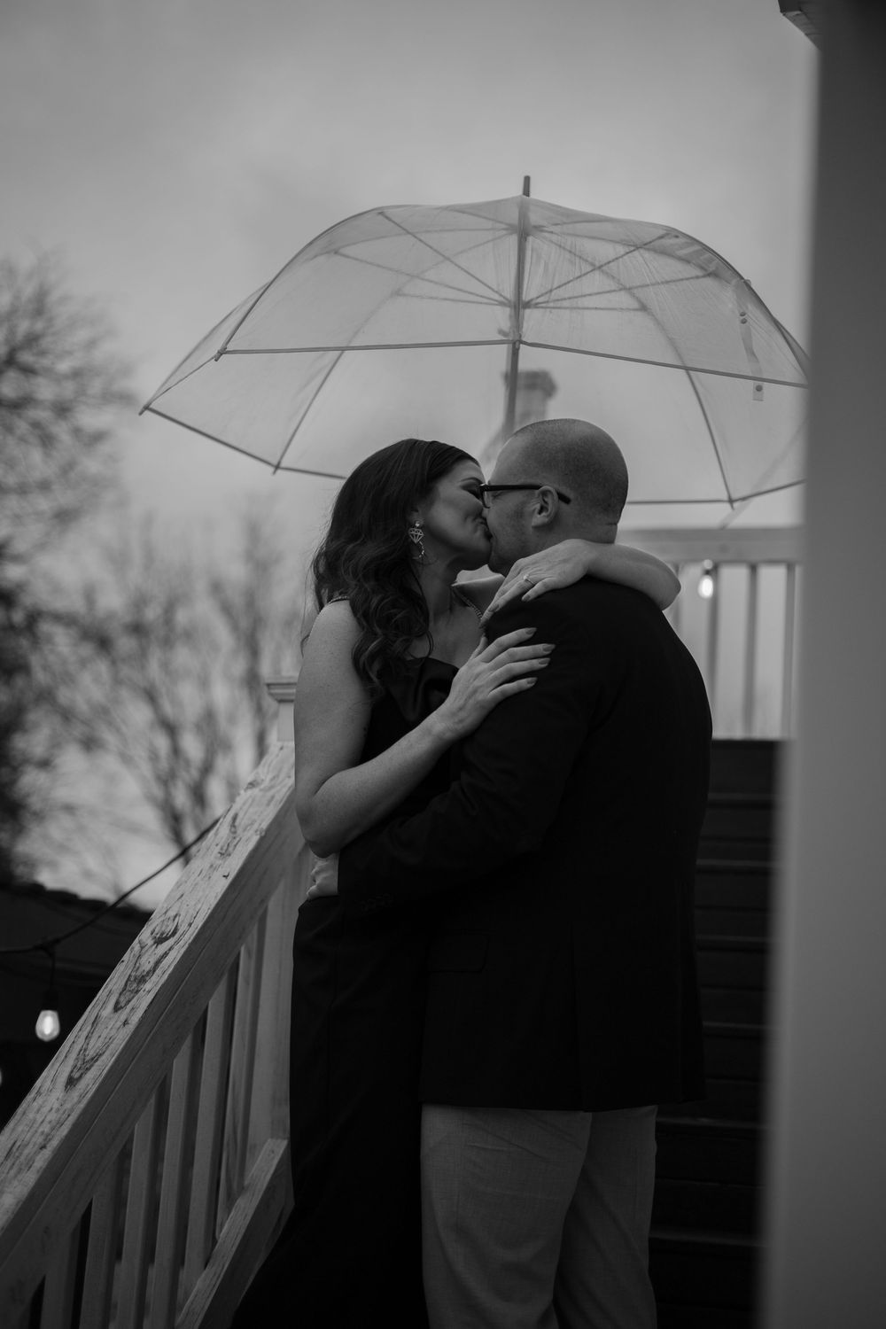 A romantic black and white portrait under a clear umbrella on a porch.