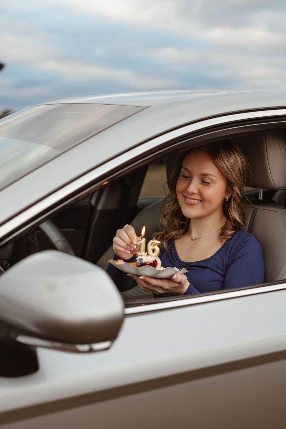 A silver car is parked while someone enjoys a snack through the driver's side window.